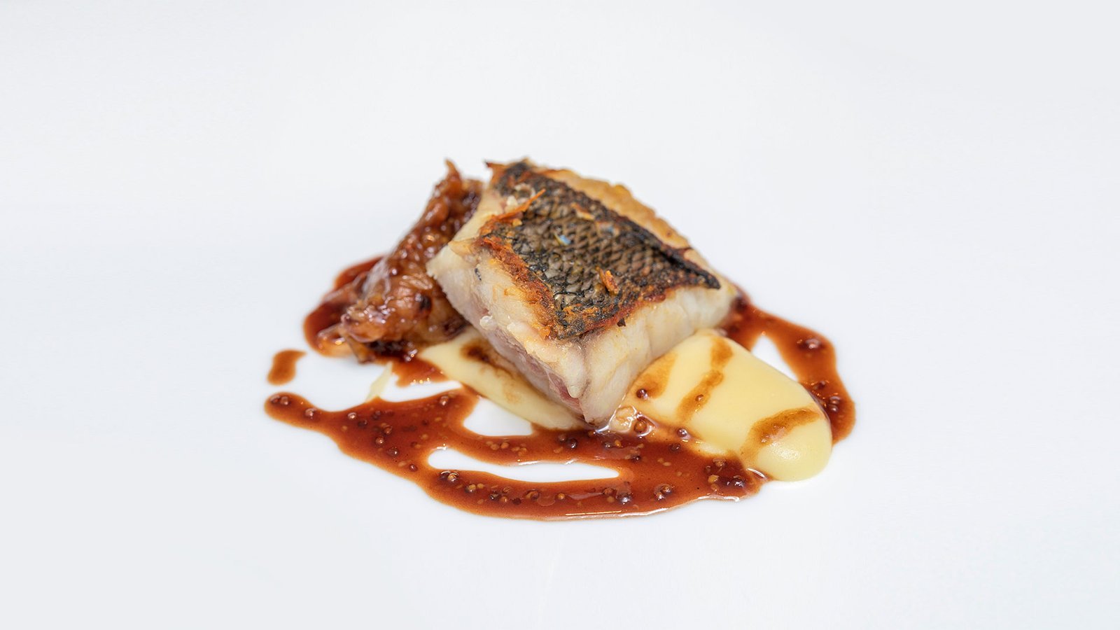 Lomo de pescado a la brasa con puré y salsa reducida.